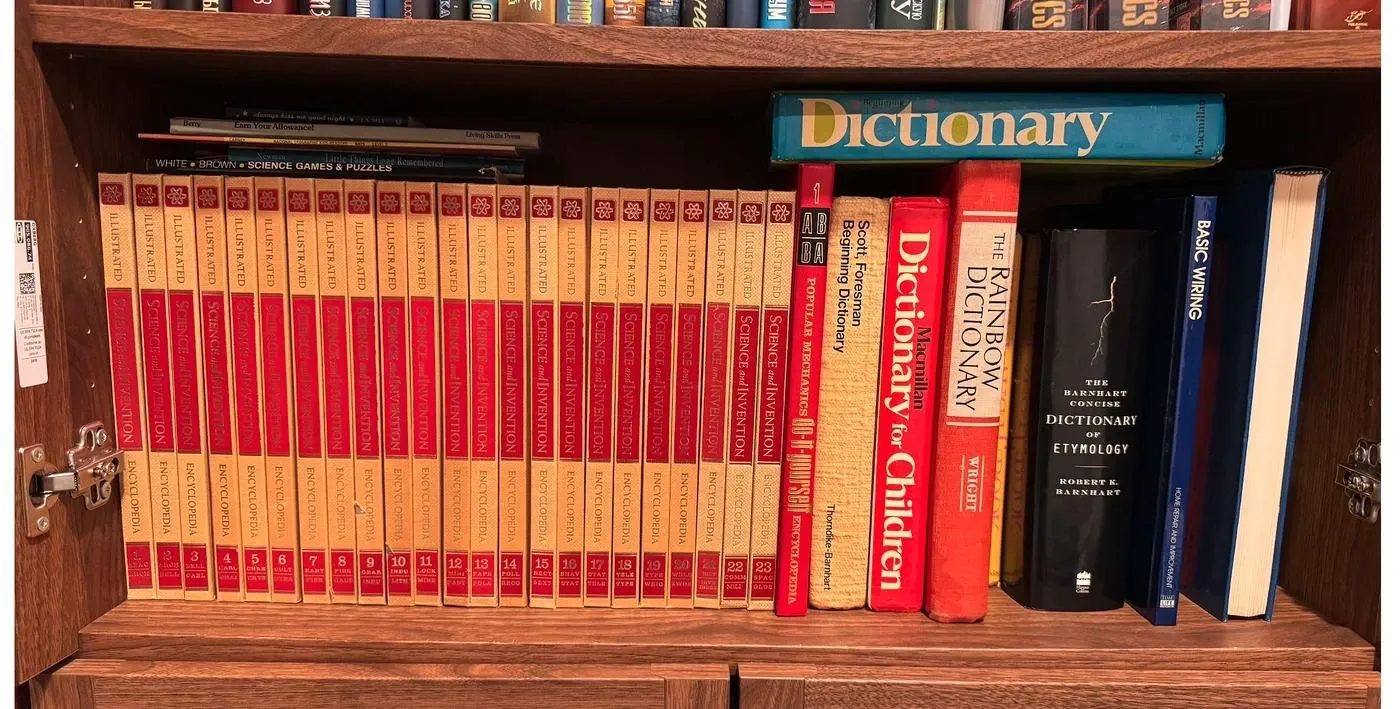 A bookshelf: twenty-three volumes of an illustrated science encyclopedia, a beginning dictionary, a dictionary for children, the Rainbow Dictionary, a dictionary of etymology, and a book on basic wiring